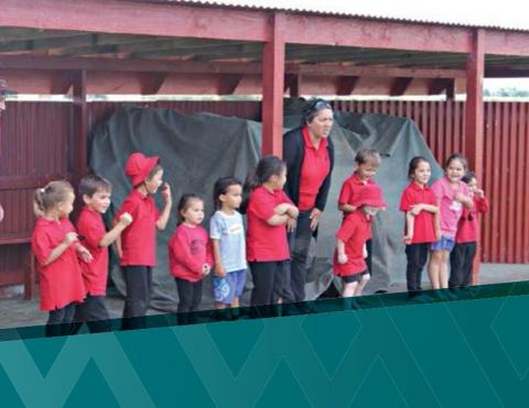 A teacher and eleven students all dressed in red shirts stand on an outdoor stage facing out