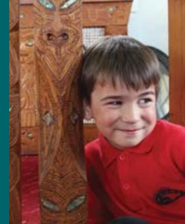 A child leans against a wooden carving with paua inlays.