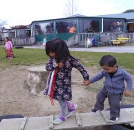 Two young children holding hands crossing a bridge on a playground.
