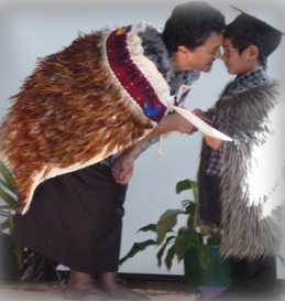 A women wearing a traditional Māori cloak hongis a young boy also wearing a traditional Māori cloak, a graduation cap and holding a piece of paper.