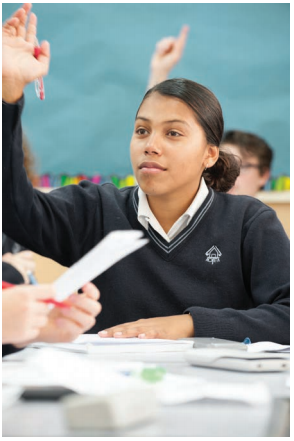 This image is a photo of a female Maori college student participating by raising her arm to answer 