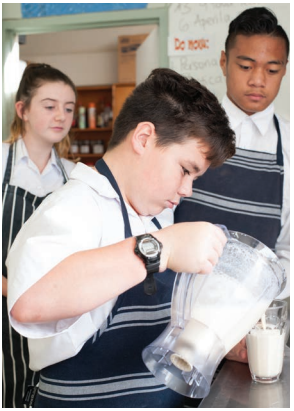 This image is a photo of three college students cooking. One female and two males. They are pouring their liquid creation into a drinking glass