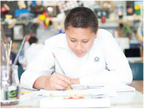 This image is a photo of a male student drawing at the art table. 